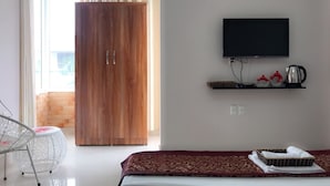 A hotel room with a bed, a TV mounted on the wall, a wooden wardrobe, and a small table with a kettle and cups. - Sky Halong Hotel (Bai Chay)