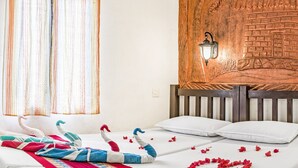 Ein Zimmer mit einem Bett, einem Holz-Kopfteil, einer Wandleuchte und einem Fenster mit gestreiften Vorhängen.