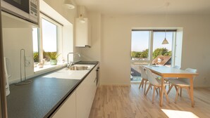 A modern kitchen with a large island, a dining area with a table and chairs, and large windows offering a view of the outdoors. - Aalborg Hotel Apartments (Aalborg)