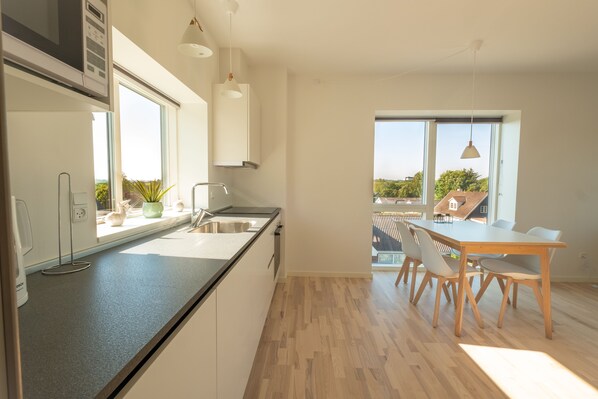 Una cocina moderna con una isla grande, un comedor con mesa y sillas, y ventanas amplias que ofrecen vistas al exterior.