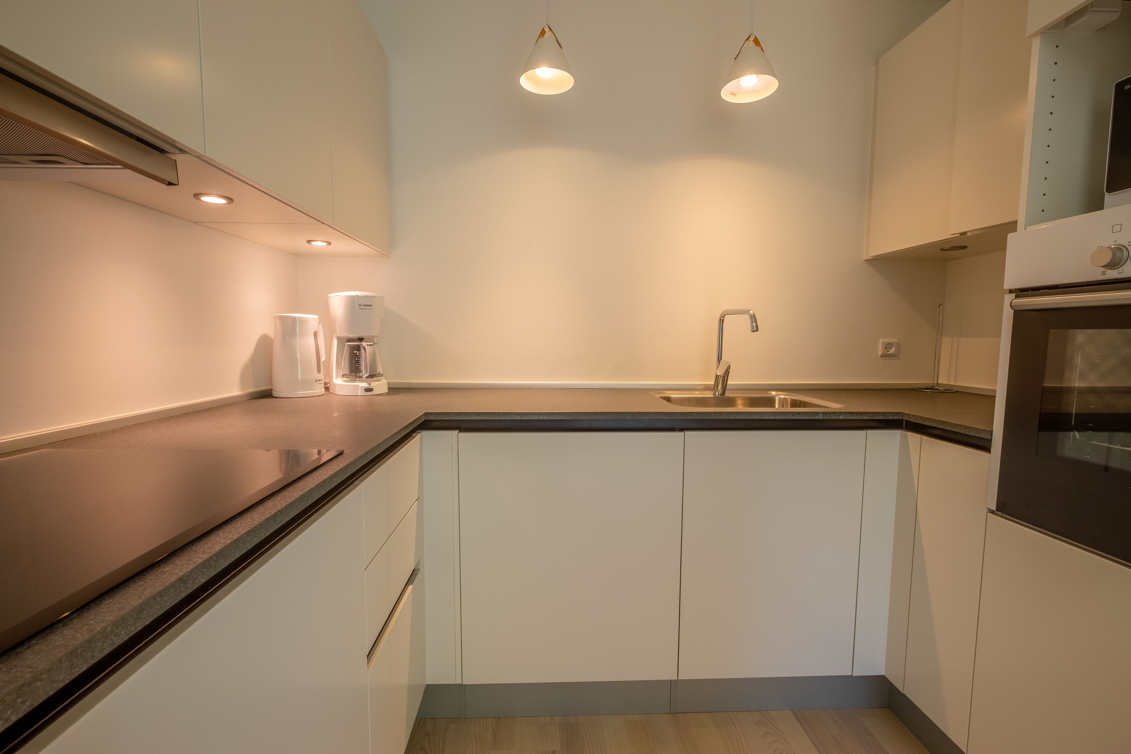 A modern kitchen with white cabinets, a black countertop, and two pendant lights.