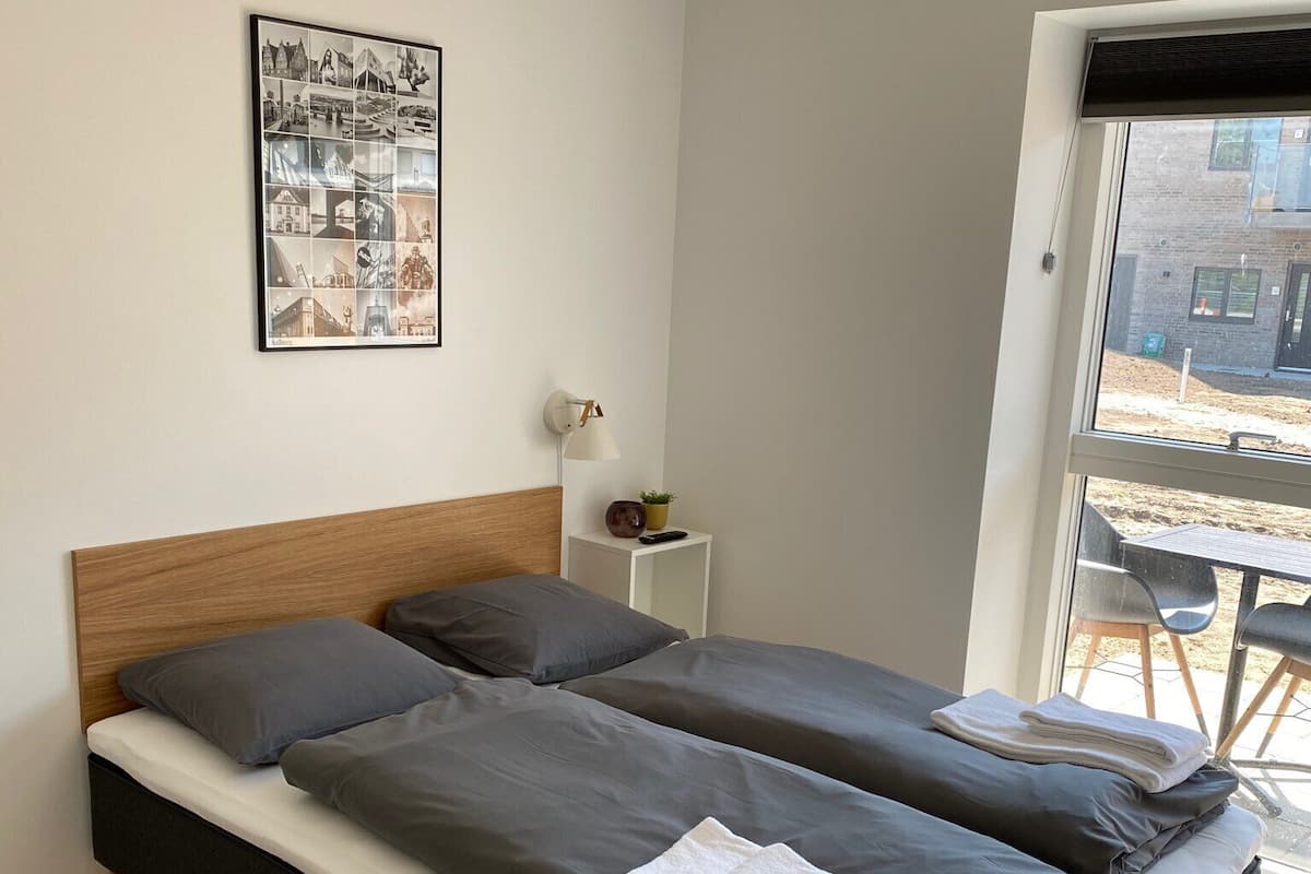 Une chambre moderne avec une tête de lit en bois, deux lits simples, une petite table de chevet avec une lampe et un tableau encadré au mur.