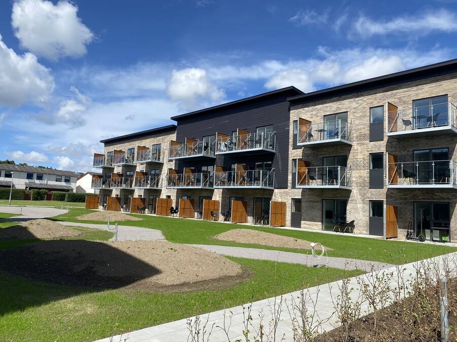 A modern apartment building with multiple balconies, a landscaped courtyard, and a clear sky.