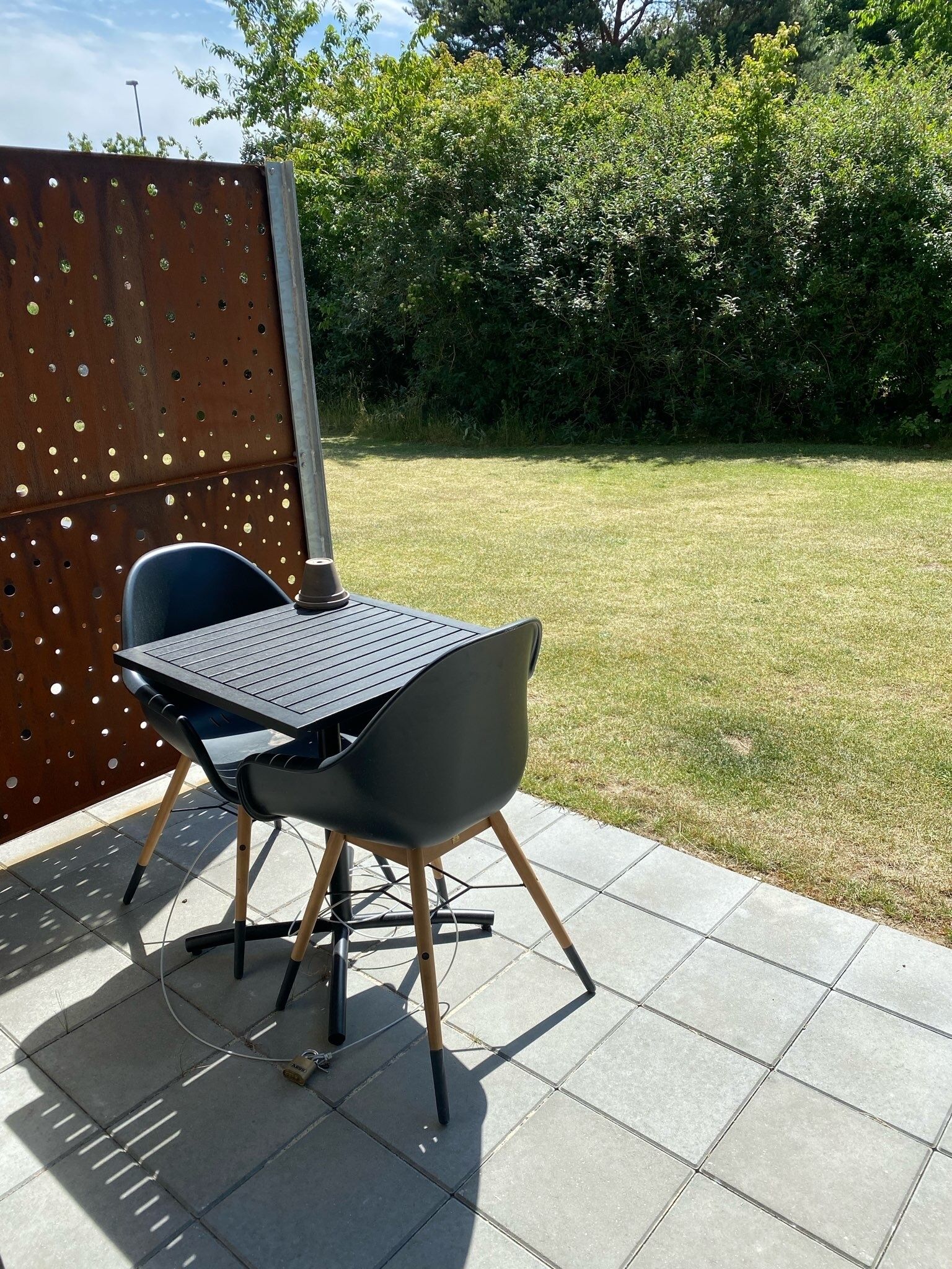 Un patio con mesa y sillas, cercado por una valla metálica y con un césped.