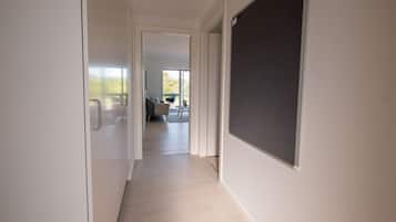 A hallway with a light wooden floor, white walls, and a large dark screen on the right.