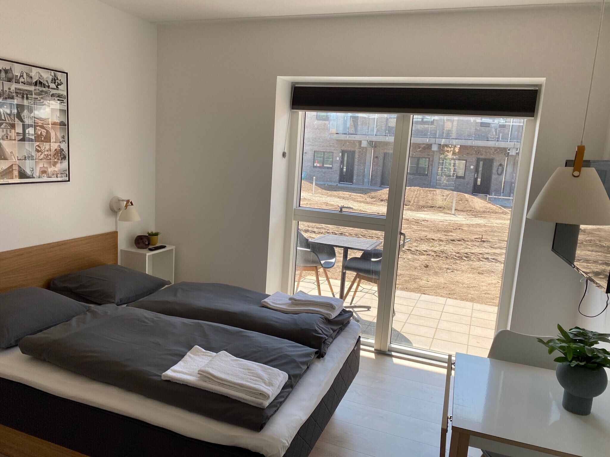 Habitación de hotel con cama, escritorio, silla, lámpara y vistas al exterior.