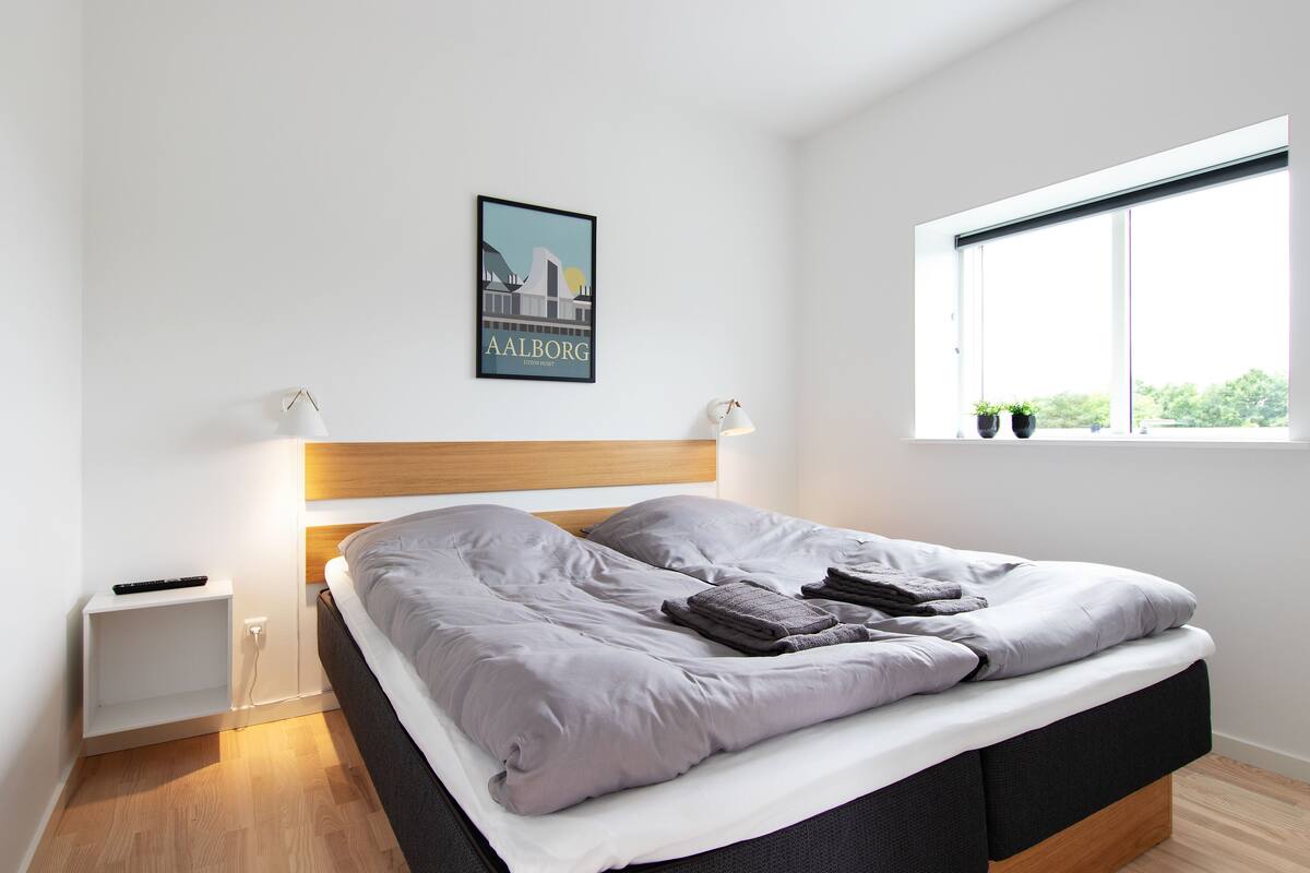 Une chambre moderne avec un lit, des lampes de chevet, une table de nuit et une fenêtre donnant sur un beau paysage.