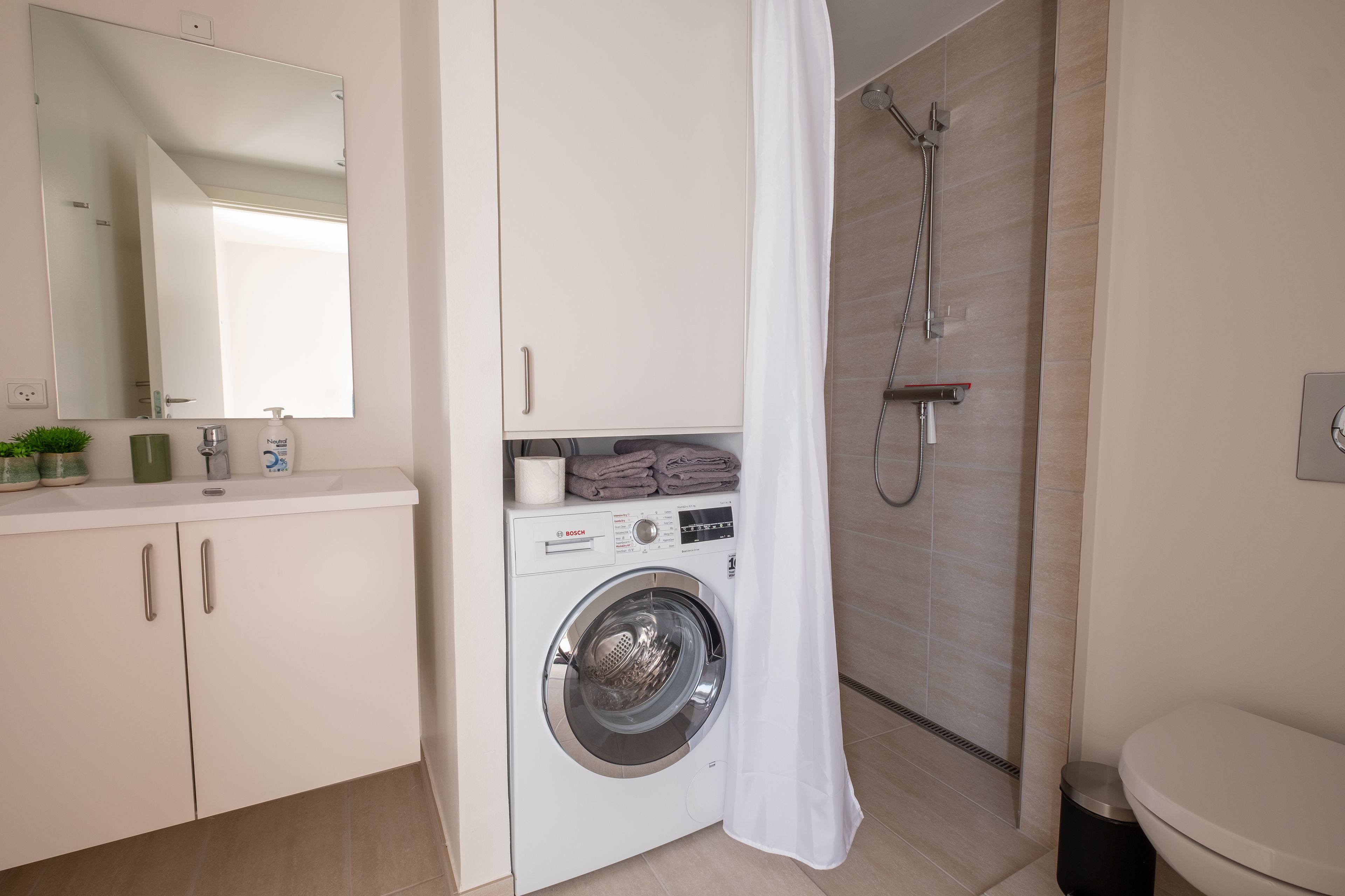 A modern bathroom with a Bosch washing machine, a shower, and a toilet.