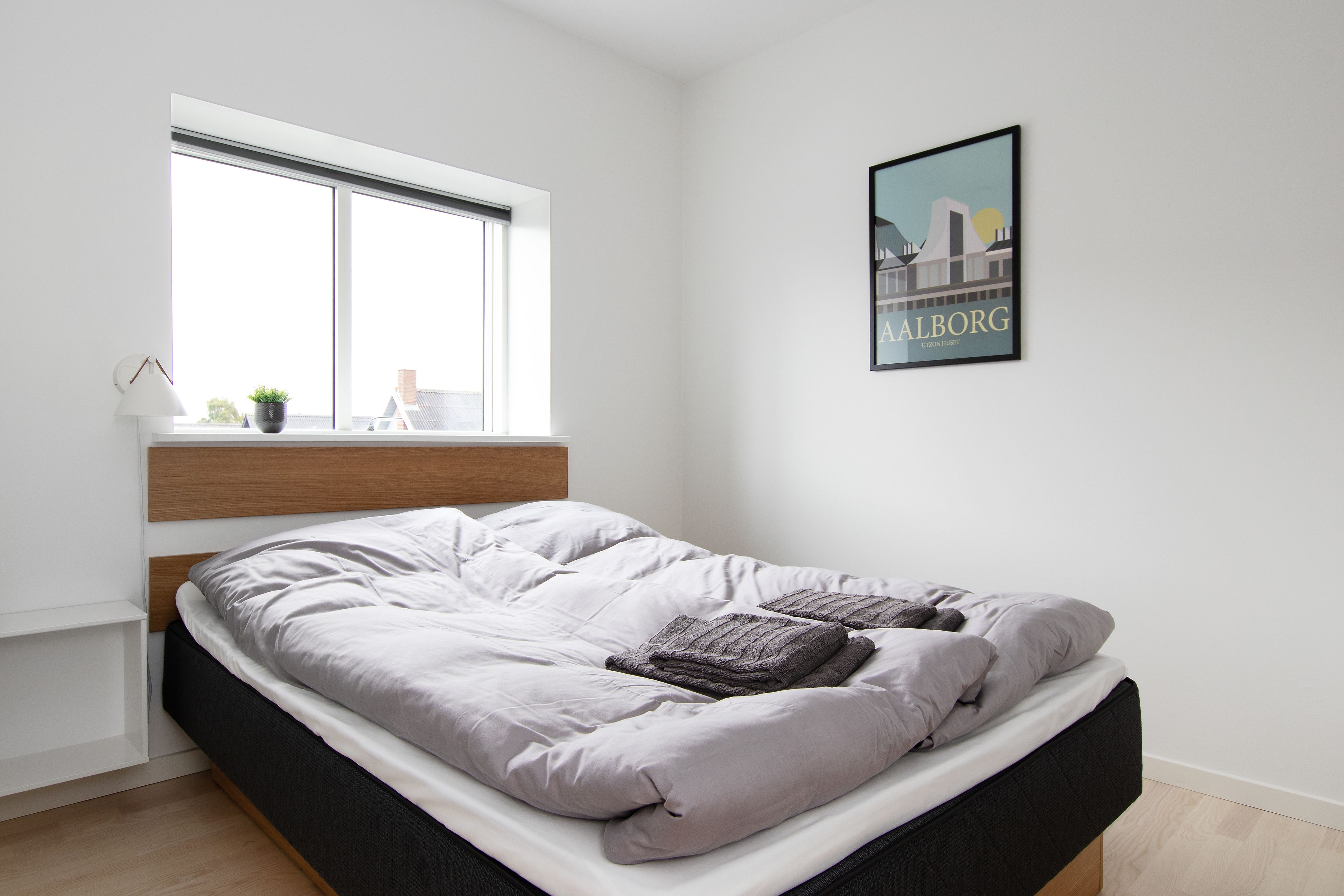 Ein modernes Schlafzimmer mit einem Bett, einem Fenster, einem Wandbild und einer kleinen Pflanze auf dem Fensterbrett.