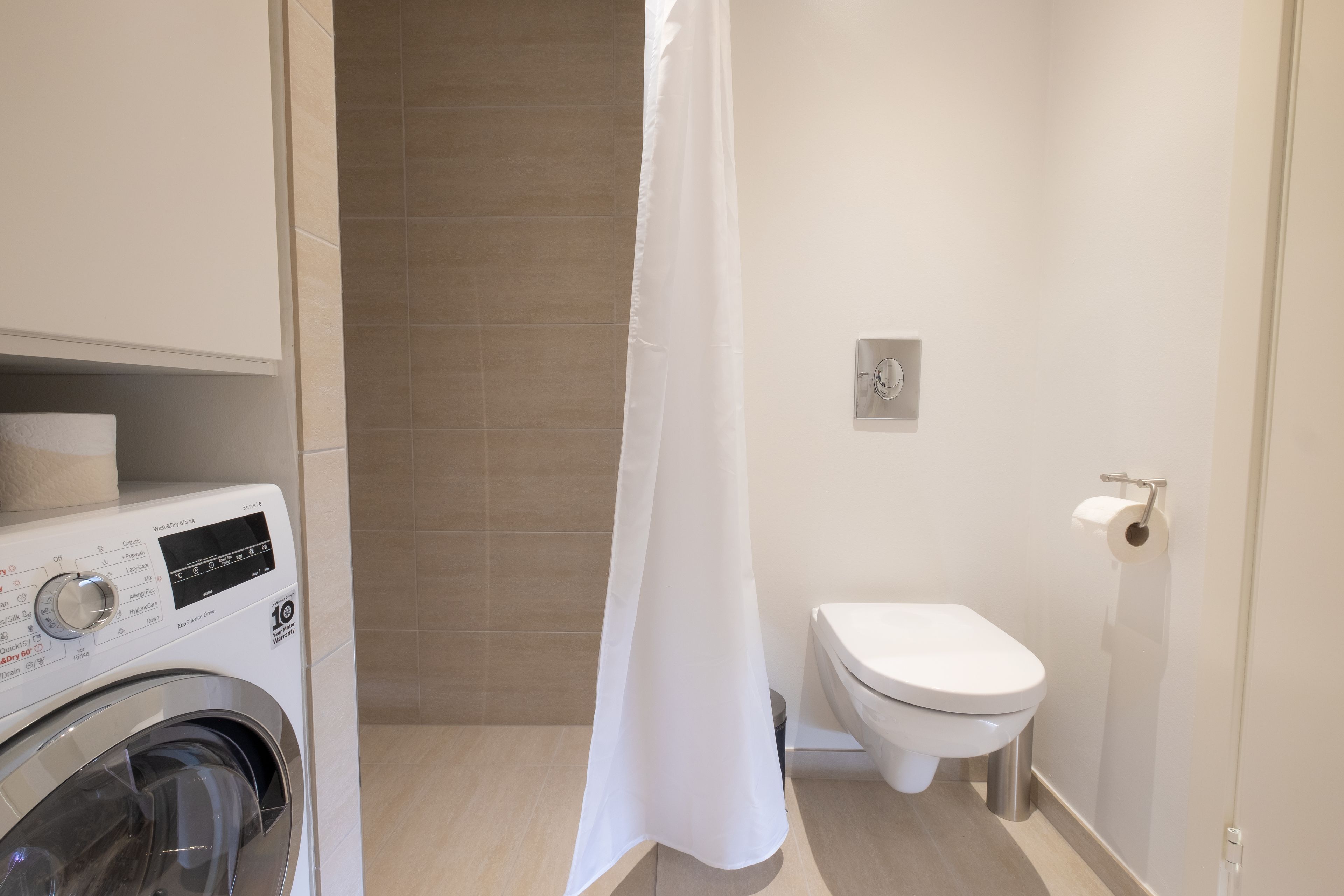 A compact bathroom with a washing machine, toilet, and shower curtain.