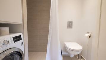 A compact bathroom with a washing machine, toilet, and shower curtain.