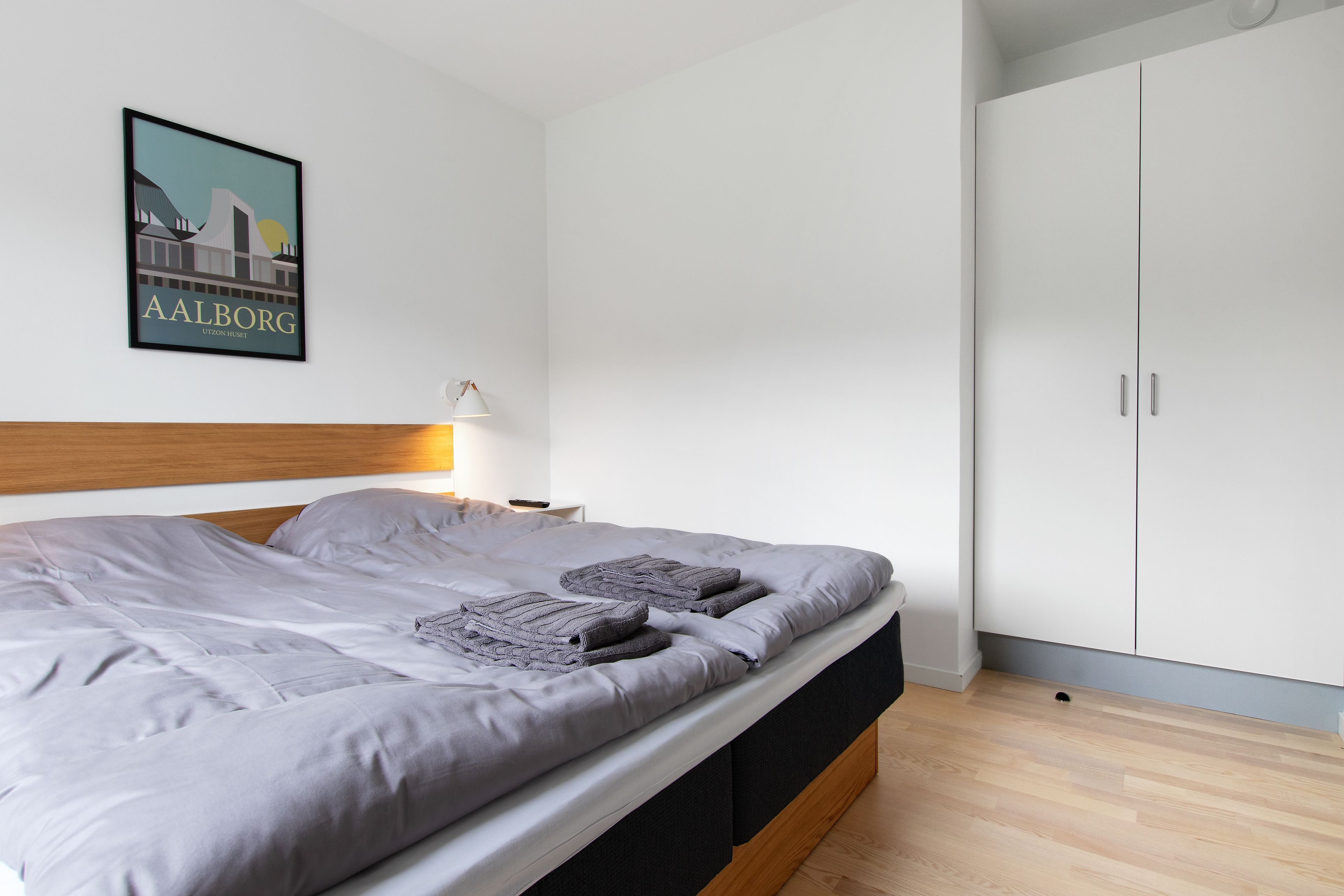A modern bedroom with a bed, a nightstand, a lamp, and a wardrobe.