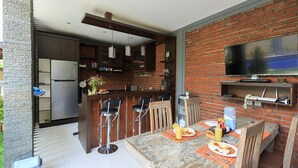 A modern kitchen with a bar area, a dining table with orange placemats, and a TV mounted on a brick wall. - Villa Twin Lovina (Banjar)