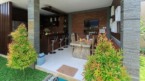 An outdoor dining area with a stone pillar, a brick wall, and a television mounted above a bar area. - Villa Twin Lovina (Banjar)
