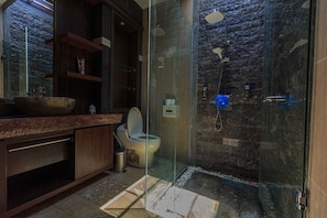 A modern bathroom with a glass-enclosed shower, a stone wall, and a wooden vanity.