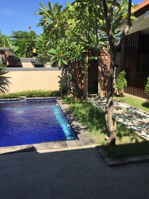 A swimming pool with a brick border, surrounded by greenery and a small waterfall feature.