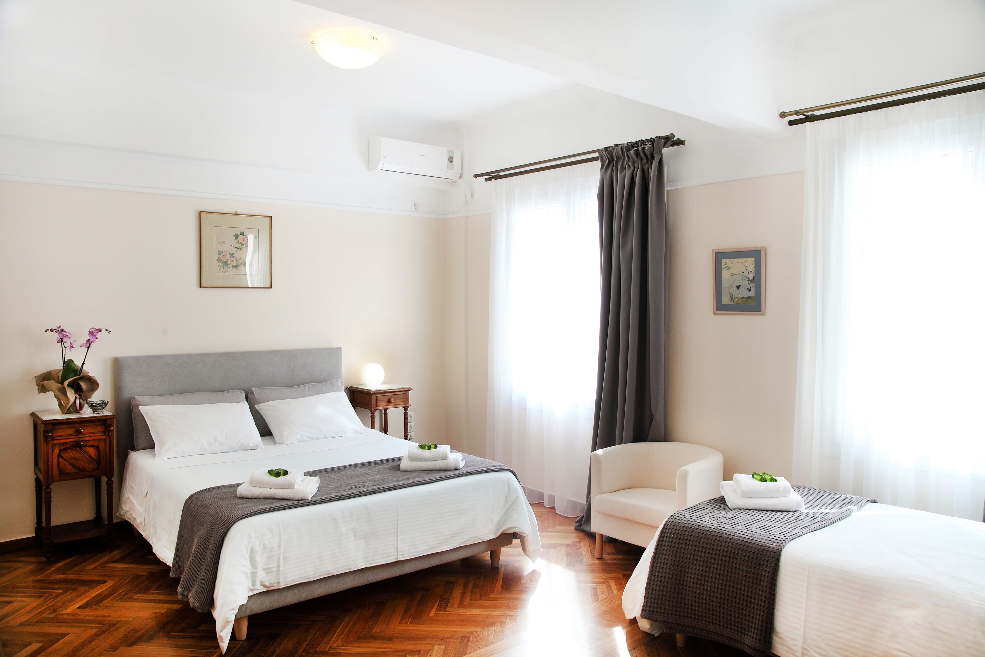 Une chambre d’hôtel avec un grand lit, une chaise et une petite table sur laquelle est posé un vase de fleurs.