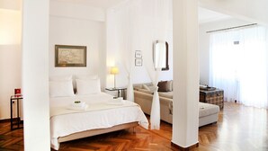 Une chambre d’hôtel avec un grand lit, une table de chevet, une lampe, un canapé et une valise.