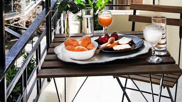Un balcon avec une table préparée pour le petit-déjeuner, comprenant des croissants, des fraises et du jus, donnant sur un panorama urbain.