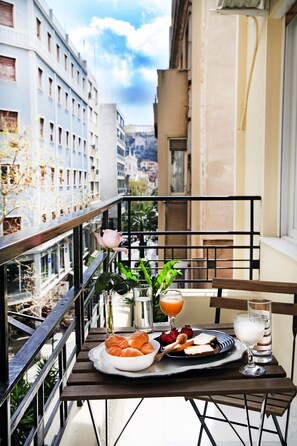 A balcony with a table set for breakfast, including croissants, strawberries, and juice, overlooking a cityscape. - My Athens House (Athens)