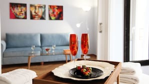 Une table à manger avec une assiette de nourriture et deux verres de vin rouge, un canapé et des tableaux abstraits accrochés au mur.