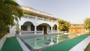 A two-story building with a swimming pool, surrounded by palm trees and a green lawn. - GuestHouser 4 BHK Bungalow 7283 (Mawal)