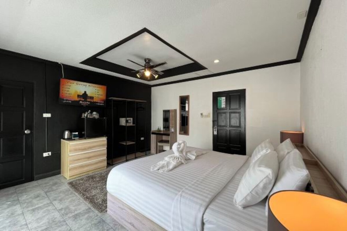 A modern hotel room with a large bed, a ceiling fan, a flat-screen TV, a wooden dresser, and a desk.