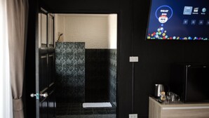 A hotel room with a dark wooden door, a white towel on the floor, a black tiled shower area, and a flat-screen TV mounted on the wall. - Big Boys' Bed & Burger (Patong)