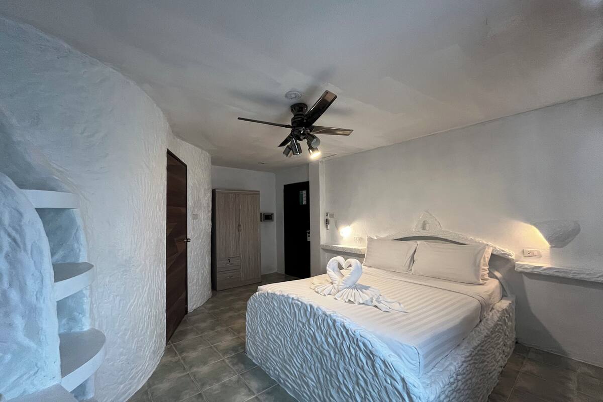 A bedroom with a bed, a ceiling fan, a wardrobe, and a staircase.