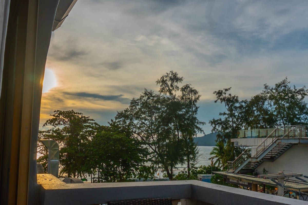 A view from a balcony overlooking a body of water, trees, and a distant mountain.