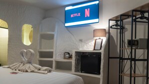 A hotel room with a bed, a TV displaying the Netflix logo, a wall-mounted shelf with a lamp, and a wardrobe with hanging clothes. - Big Boys' Bed & Burger (Patong)