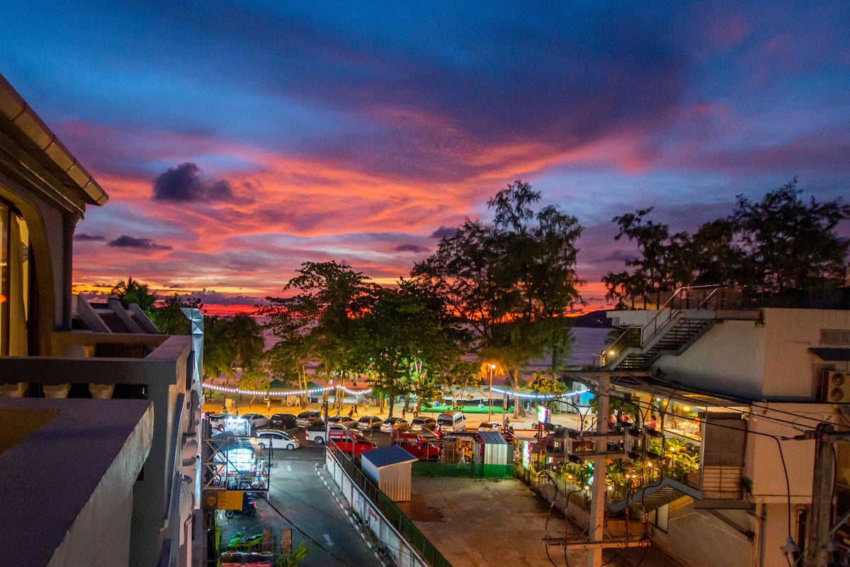 A street view at dusk with a sunset sky, street lights, and parked cars.
