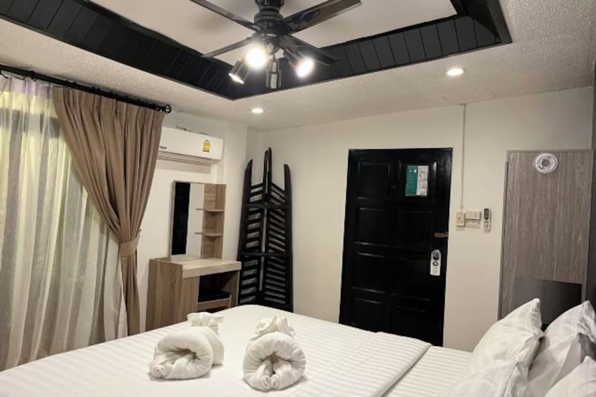 A hotel room with a bed, a ceiling fan, a wardrobe, and a door.