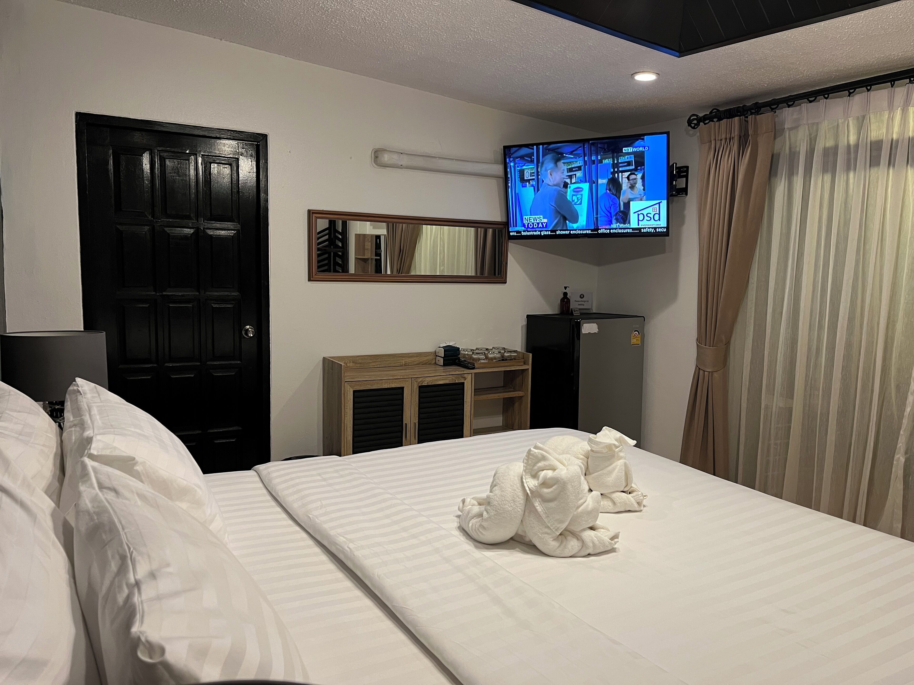 A hotel room with a bed, a television mounted on the wall, a wardrobe, and a door.