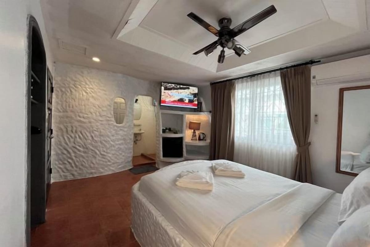 A hotel room with a bed, a ceiling fan, a television, and a bathroom.