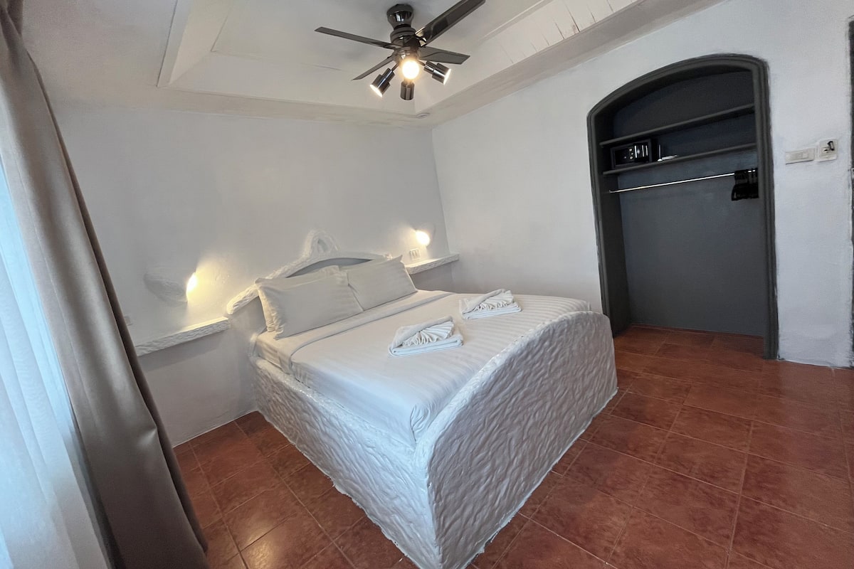 A bedroom with a bed, a ceiling fan, a nightstand, and a door.