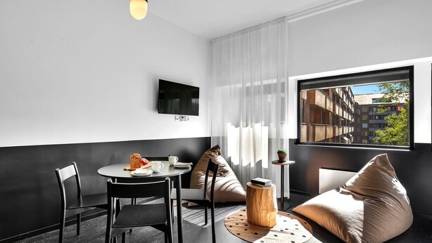 Una habitación moderna con una mesa redonda, dos sillas, un sofá, un televisor y una ventana con vista a la ciudad.