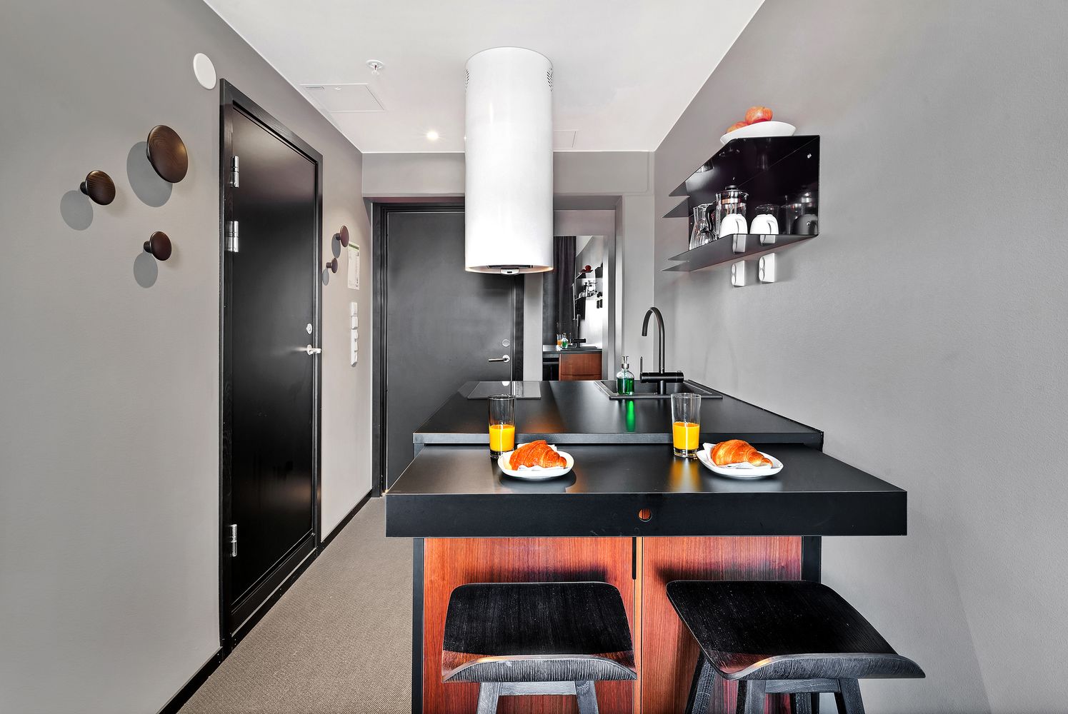 Una cocina moderna con una isla central, taburetes de bar y un estante empotrado con utensilios de cocina.