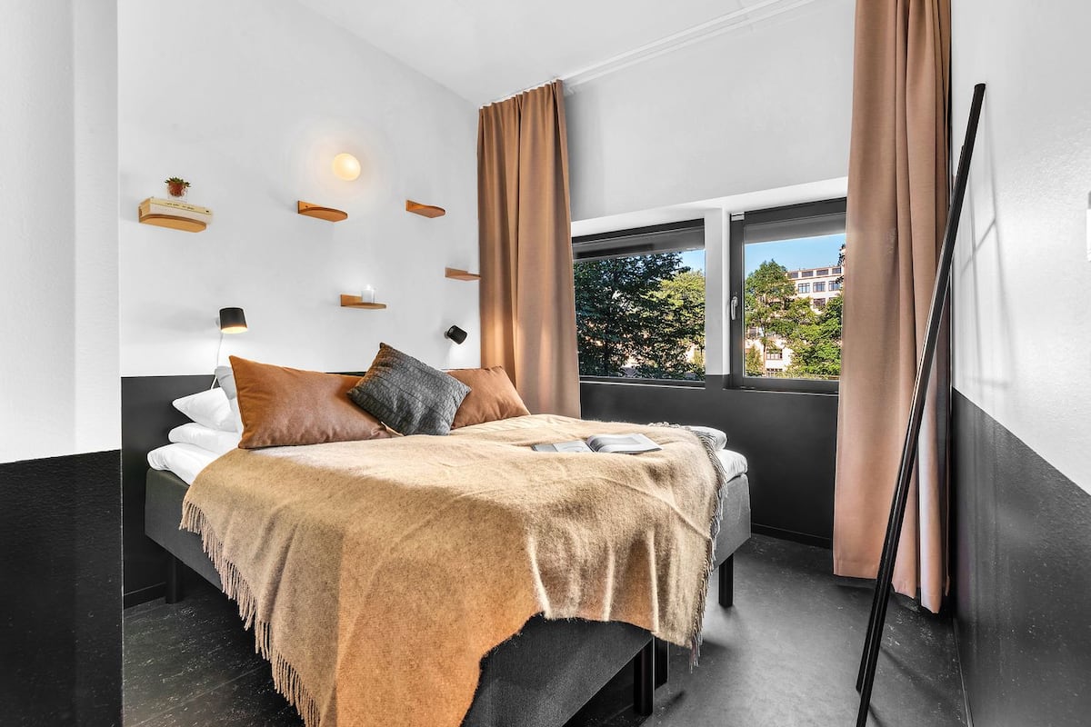 A modern bedroom with a bed, a window, and a view of buildings outside.