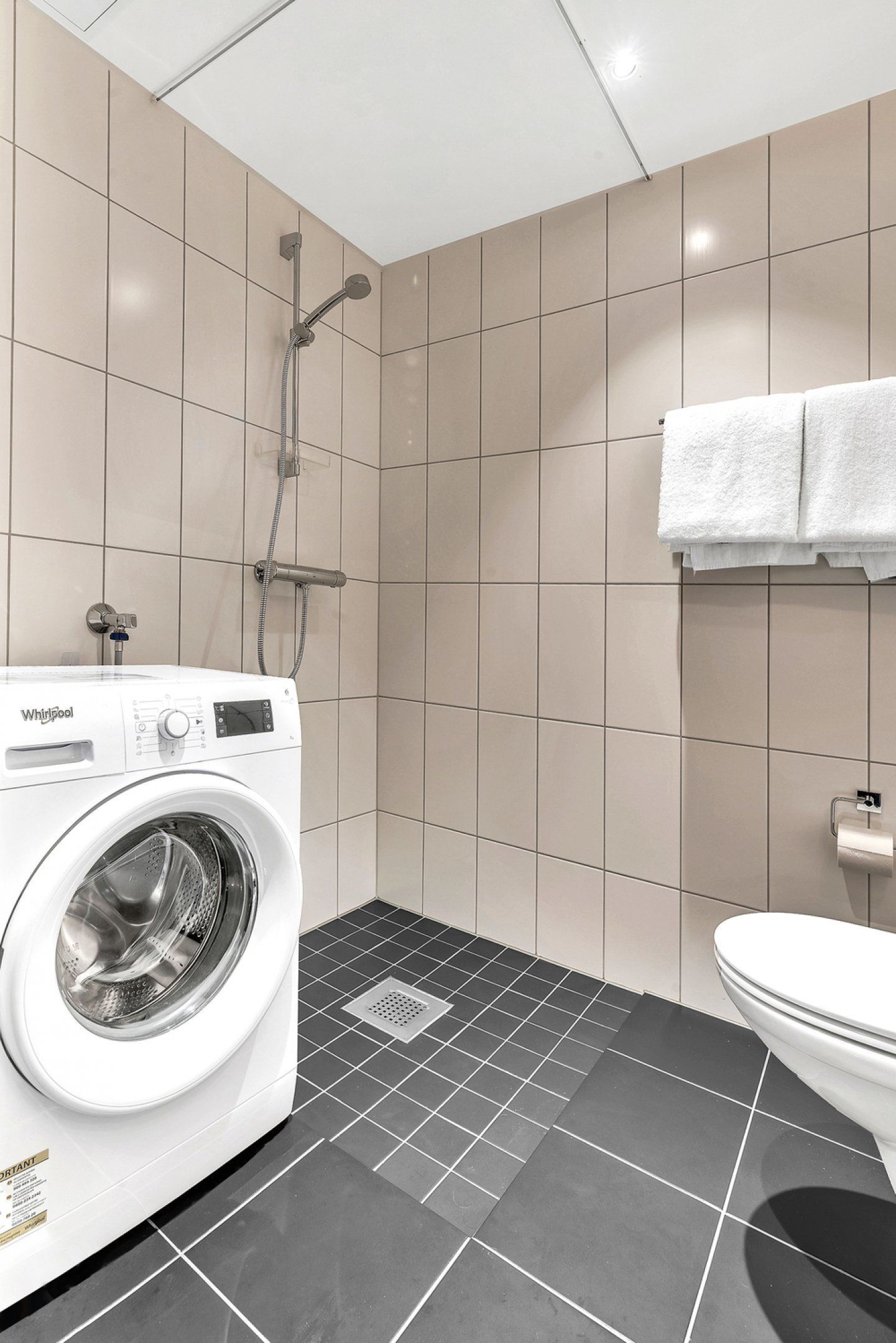A compact bathroom with a washing machine, a shower, and a toilet.