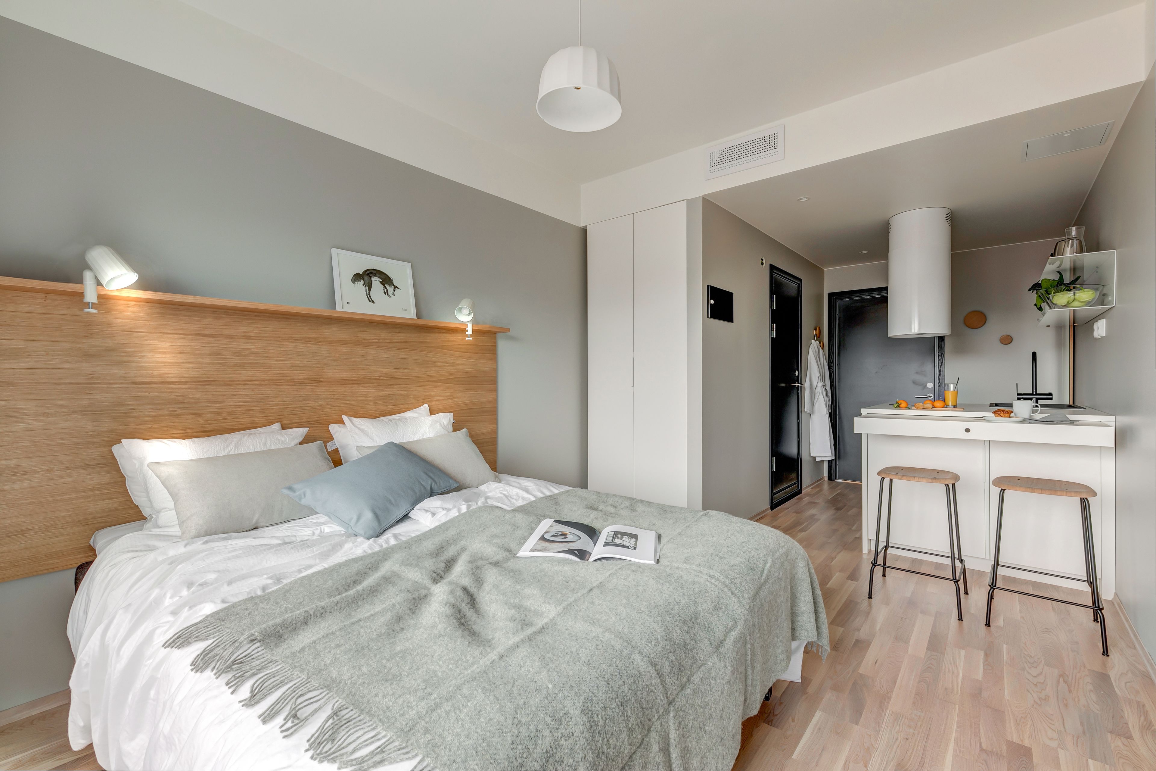 Et moderne soveværelse med sengegavl i træ, et natbord med lampe, og en seng med gråt tæppe.