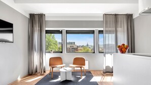 Una habitación moderna con dos sillas, una mesita y vistas a un paisaje urbano a través de amplios ventanales.