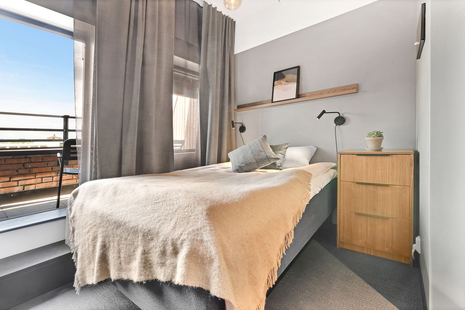 Una camera da letto moderna con un letto, un comodino in legno, una piccola pianta in vaso e vista sull'esterno.