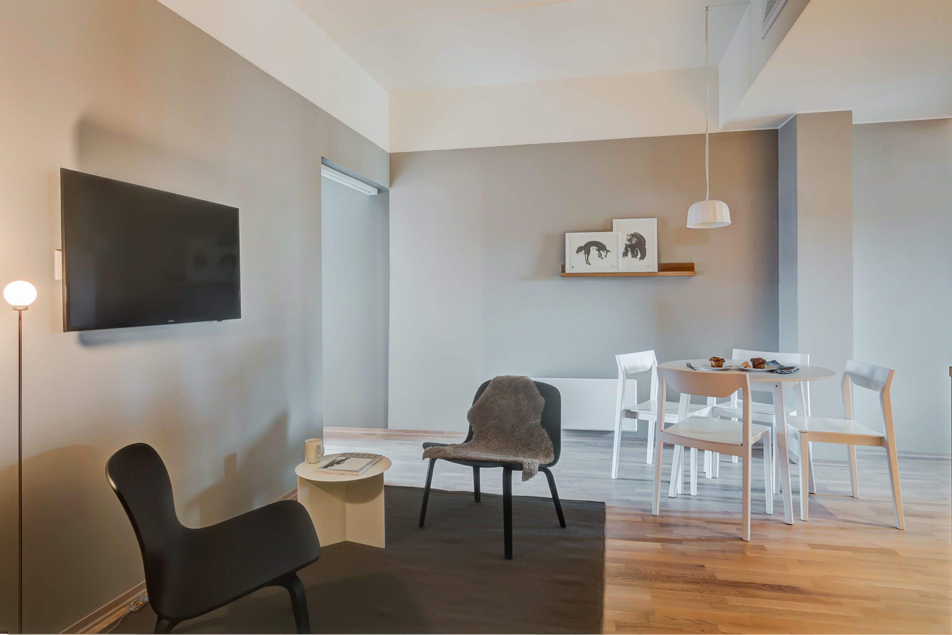 Una sala de estar moderna con un televisor de pantalla plana, una mesa de centro redonda, un sofá y un comedor con sillas blancas.