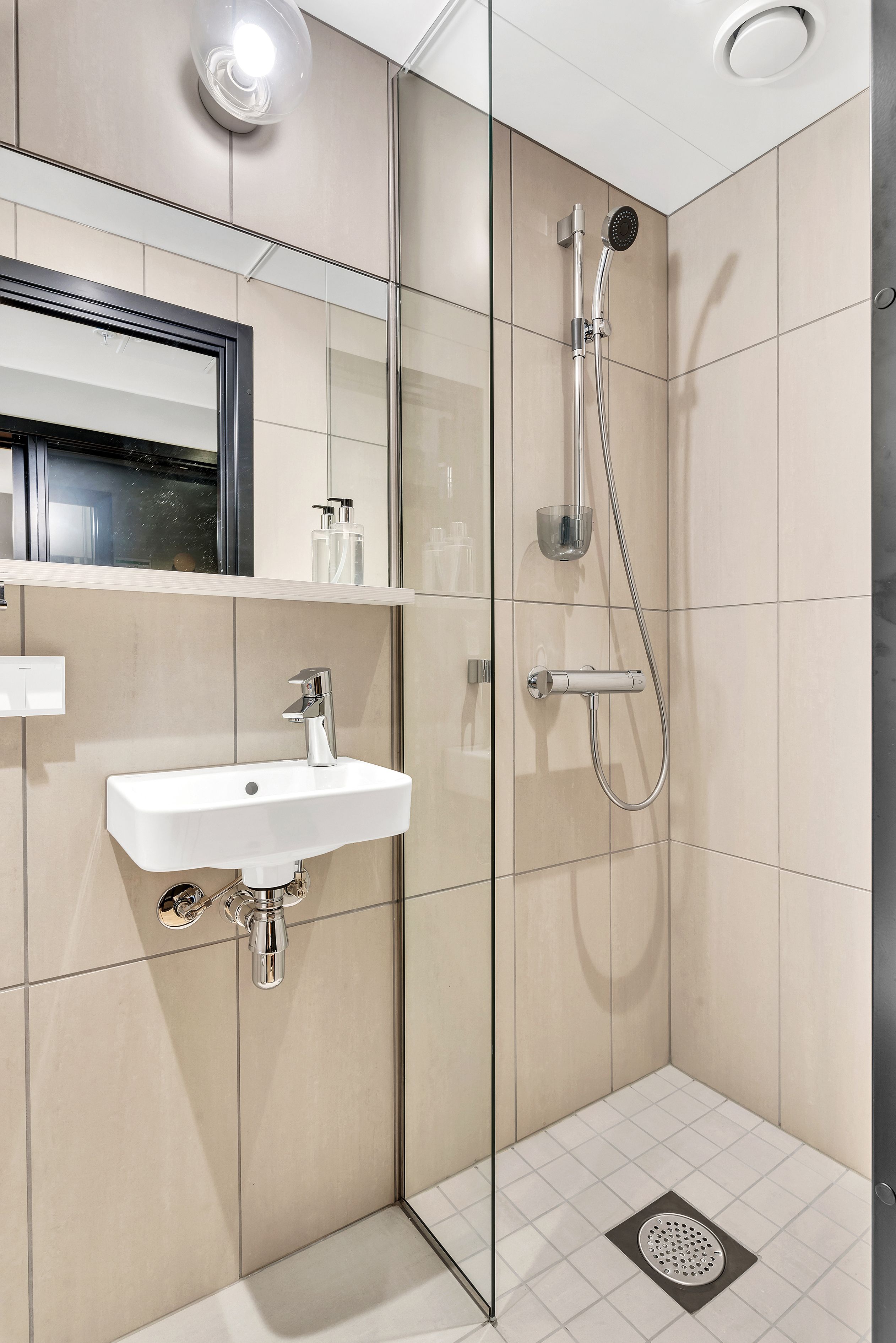 A modern bathroom with a glass-enclosed shower, a white sink, and a mirror above it.