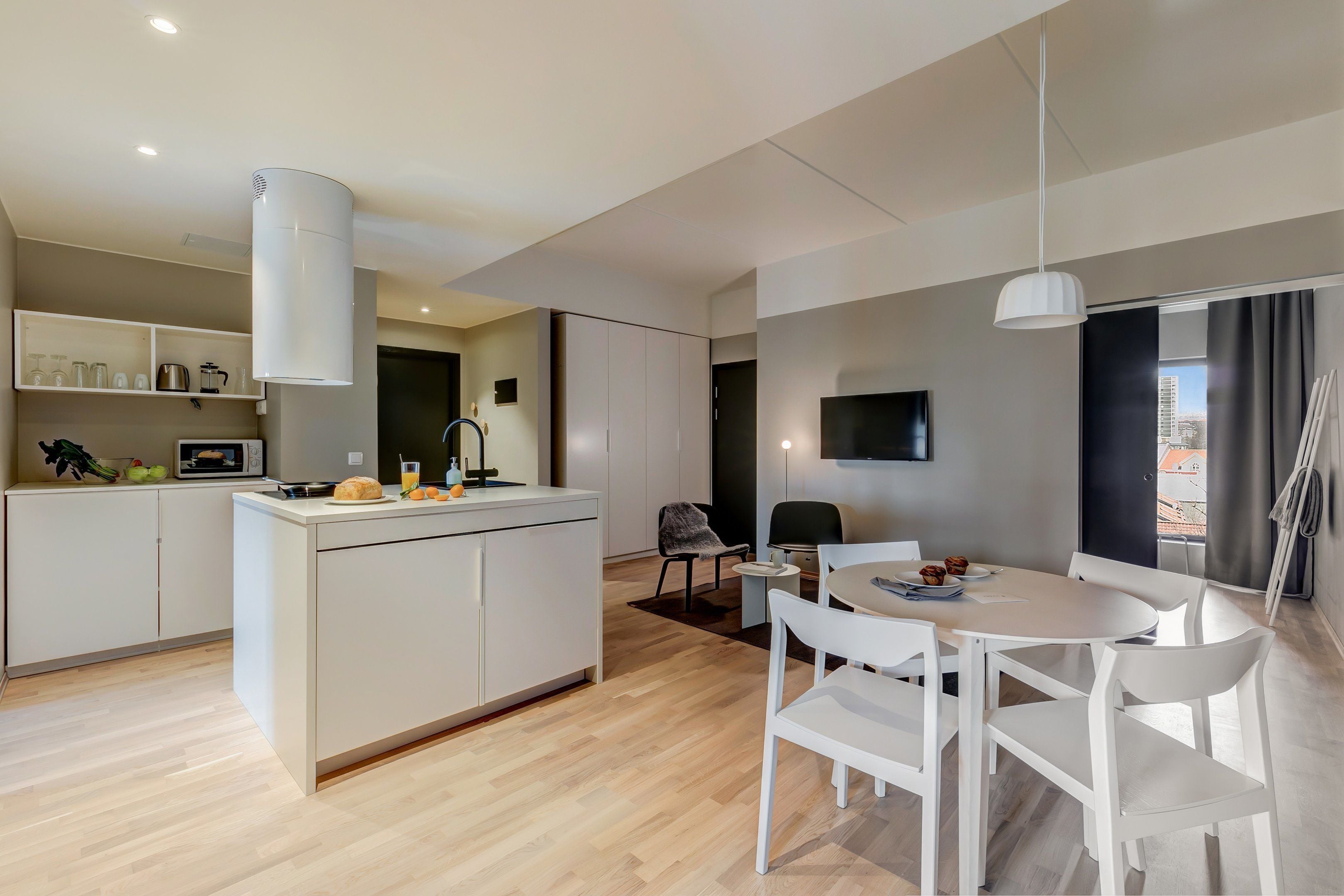 Una cocina moderna con armarios blancos, una isla central y un comedor con una mesa y sillas blancas.