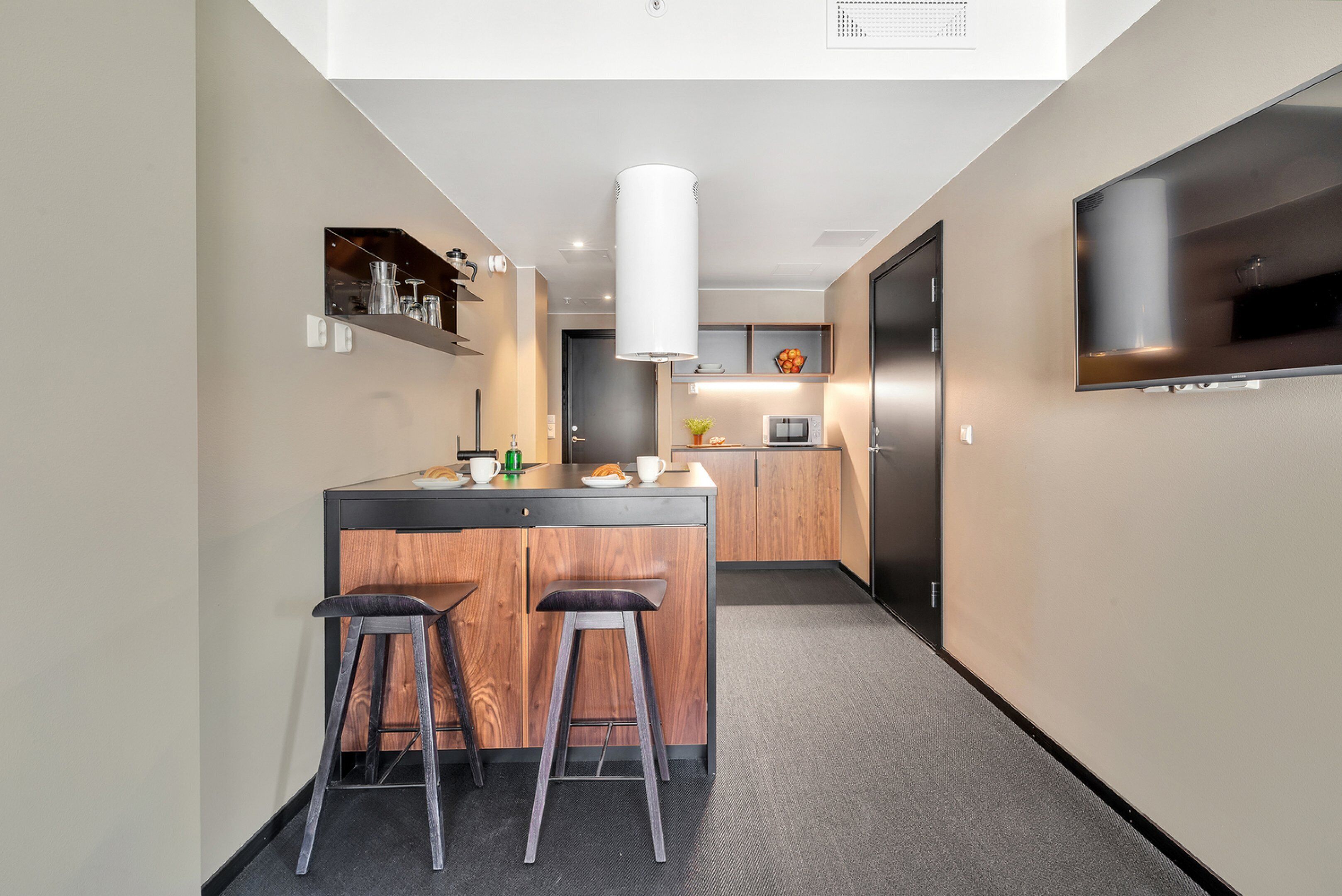 A modern kitchen with a central island, bar stools, a microwave, and a large TV mounted on the wall.