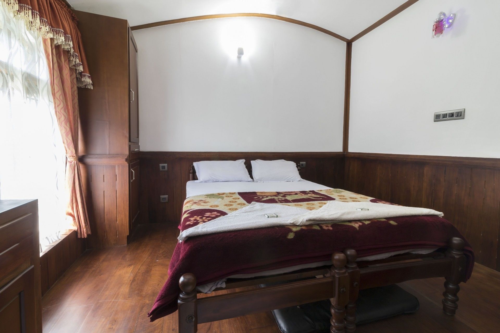 A bedroom with a wooden bed, white pillows, a patterned bedspread, and a wooden wardrobe.