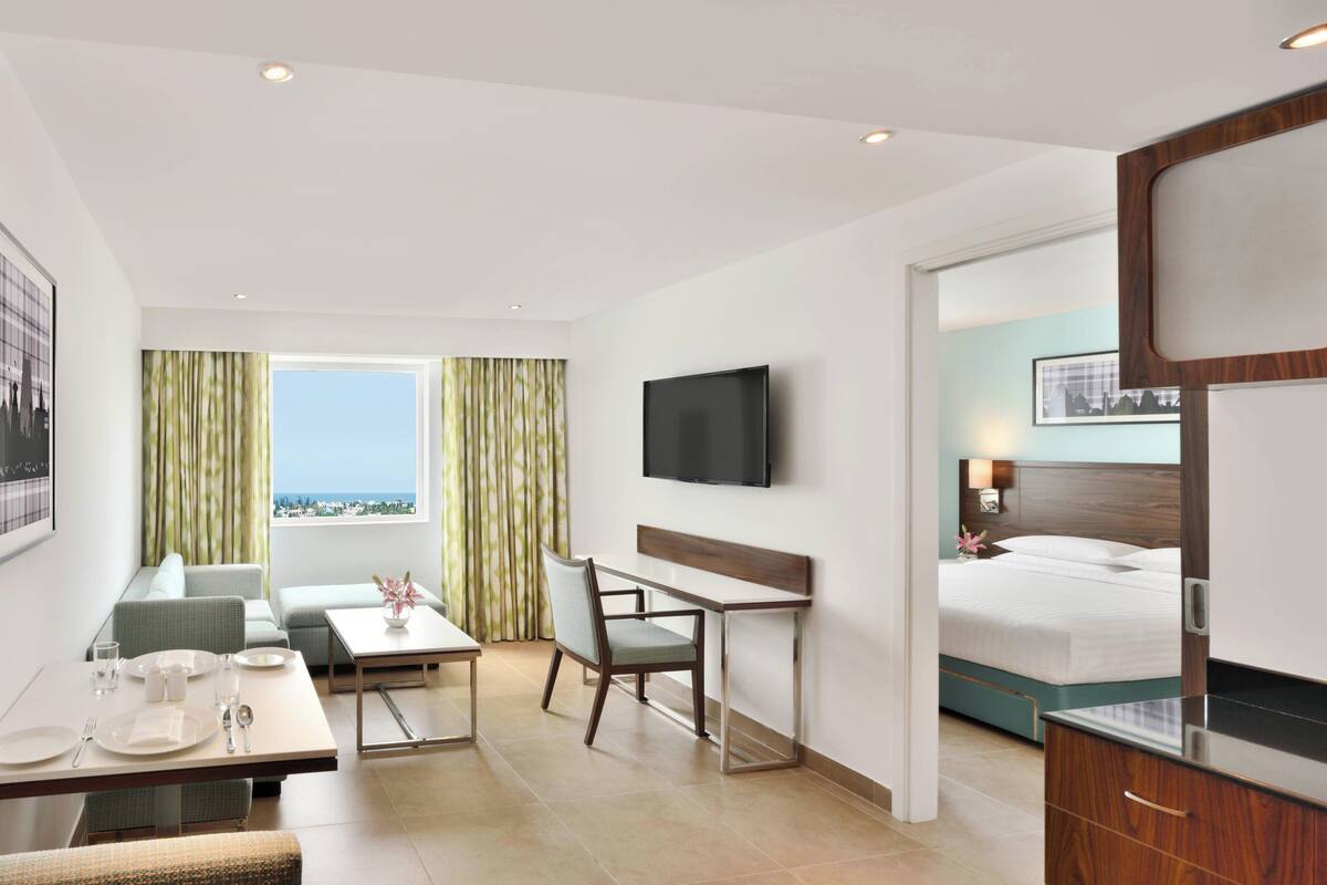Une chambre d’hôtel avec un lit, un bureau, une chaise, une télévision et une vue sur la ville.
