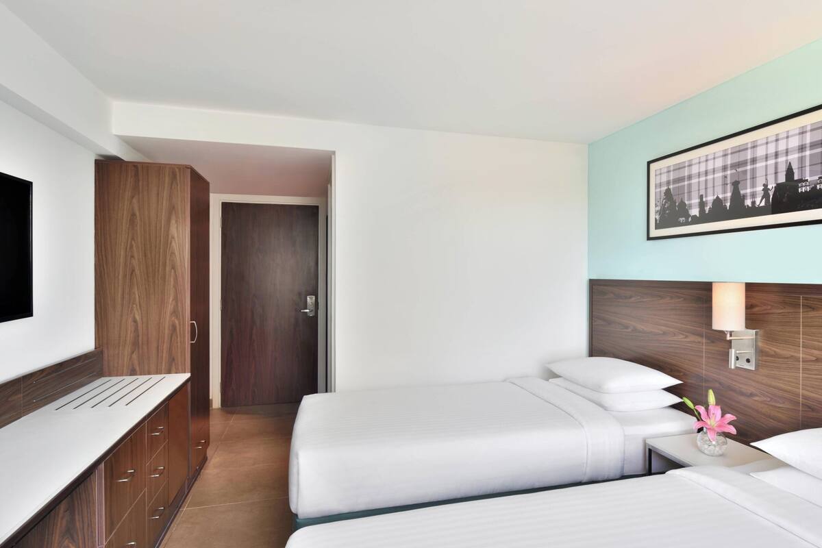 Une chambre d’hôtel avec deux lits, un bureau, une télévision et un tableau encadré au mur.